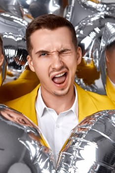 happy winking man in yellow jacket with a lot of silver air balloons. birthday party