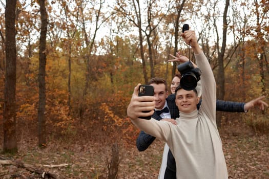 wedding photographer with bride and groom taking selfie with mobile phone in nature