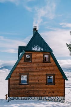 Smoke curls over the chimney of a two-story wooden cottage in a snowy village. High quality photo