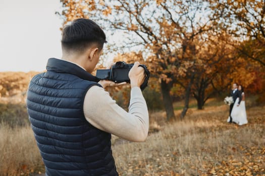 Professional wedding photographer taking pictures of the bride and groom in nature in autumn