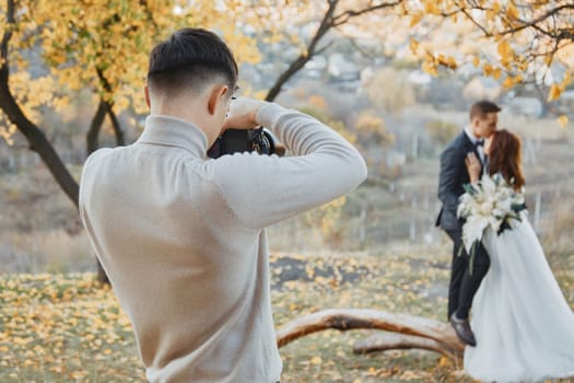 Professional wedding photographer taking pictures of the bride and groom in nature in autumn