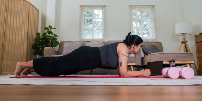Asian overweight woman doing stretching exercise at home on fitness , online fitness class. Stretching training workout on yoga mat at home for good health and body shape.