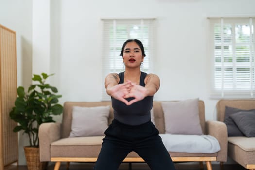 Overweight woman enjoying a fitness workout at home. Fat, plump woman and squatting on an exercise mat in the living room.