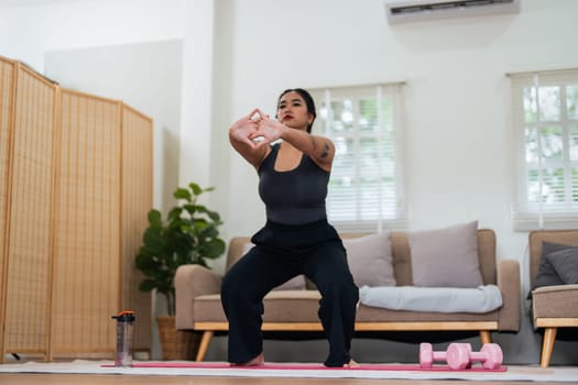 Overweight woman enjoying a fitness workout at home. Fat, plump woman and squatting on an exercise mat in the living room.