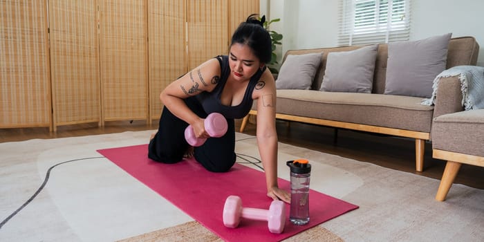 Happy fat overweight woman wearing sportswear doing fit exercise with dumbbells in living room at home. Workout sport, fitness and body concept.