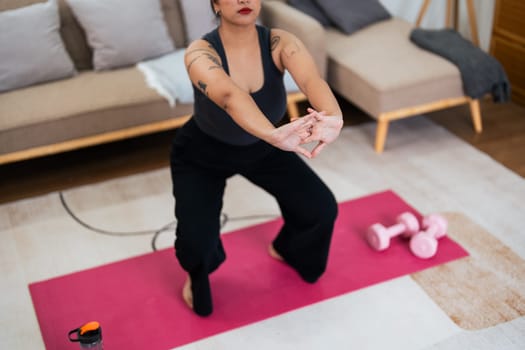 Overweight woman enjoying a fitness workout at home. Fat, plump woman and squatting on an exercise mat in the living room.