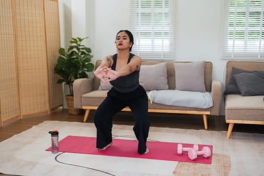 Overweight woman enjoying a fitness workout at home. Fat, plump woman and squatting on an exercise mat in the living room.