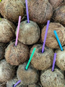 Background of coconut nuts with plastic drinking tubes, vertical frame.