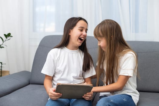 Young twins using a laptop and a tablet sitting on a couch in the living room. High quality photo