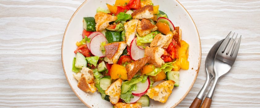 Traditional Levant dish Fattoush salad, Arab cuisine, with pita bread croutons, vegetables, herbs. Healthy Middle Eastern vegetarian salad, rustic wooden white background top view.