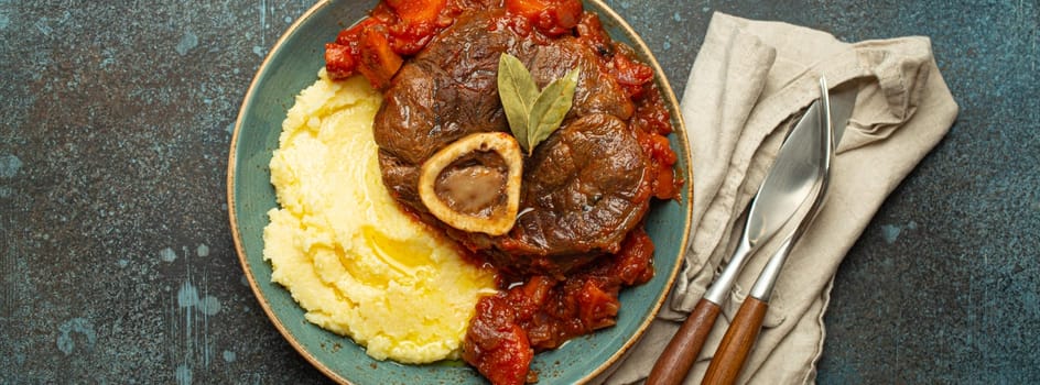 Traditional Italian dish Ossobuco all Milanese made with cut veal shank meat with vegetable tomato sauce served with corn polenta on ceramic plate top view on rustic stone background.