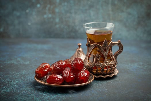 Breaking fasting with dried dates during Ramadan Kareem, Iftar meal with dates and Arab tea in traditional glass, angle view on rustic blue background. Muslim feast.