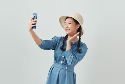 A woman takes a selfie on the phone against the white background in summer.