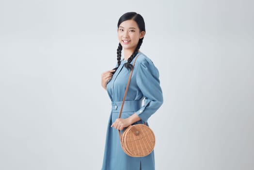 Elegant happy smiling woman wearing trendy denim dress, with small shoulder round wicker bag