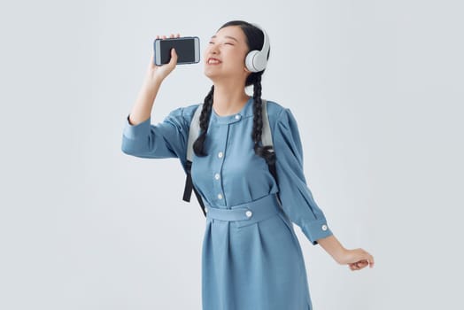 Beautiful young asian woman standing isolated, listening to music with headphones, singing