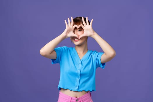Happy beautiful girl showing heart gesture with fingers isolated over purple background