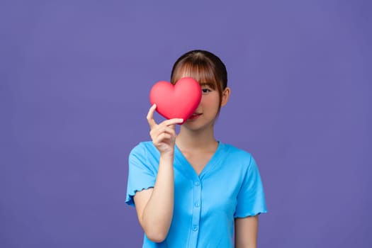 Smiling woman holding red heart on purple background