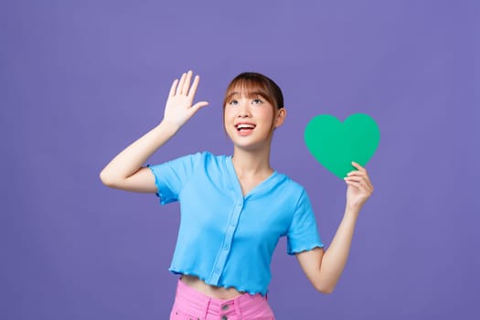 Photo of positive cute woman rising color paper heart empty space isolated purple background