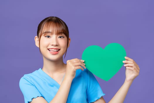 Cheerful young woman hold hands green heart paper shape isolated on purple background