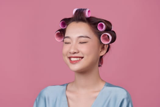 Attractive smiling girl with hair curlers on head curling hair for perfect curls