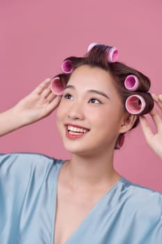 Pensive young woman in hair curlers posing on pink background