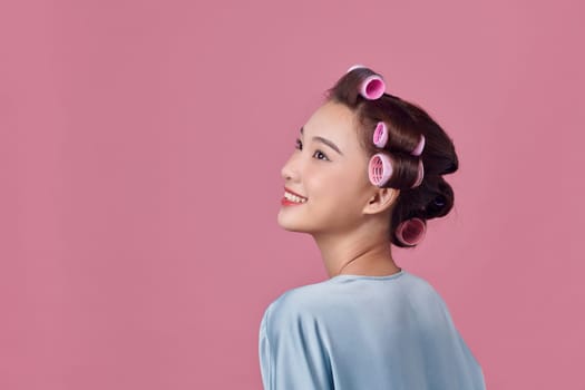 Young woman is daydreaming while wearing hair rollers, isolated over white
