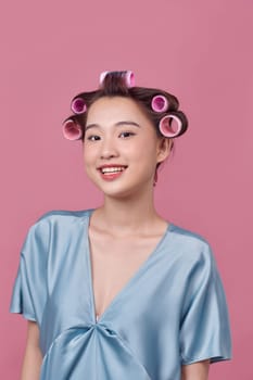 Cheerful young model posing with hair curlers on pink background