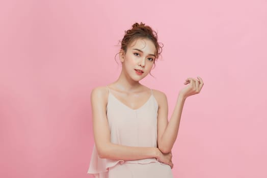 A smiling attractive woman in summer dress posing isolated over pink background