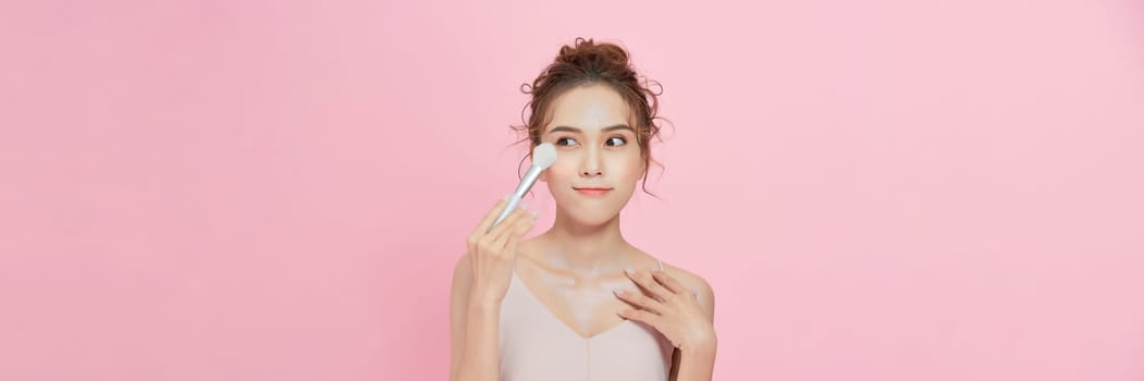 Woman applies powder on the face using makeup brush. 