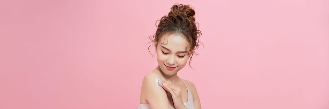 Young woman applying body cream onto shoulder on pink background