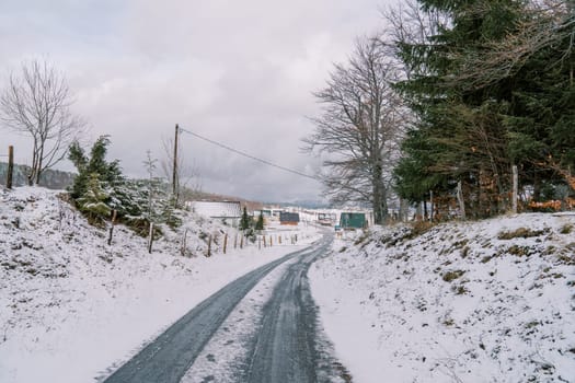 Highway through snowy forest to village with colorful houses in mountain valley. High quality photo