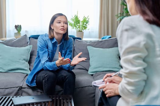 Sad young woman at therapy session with psychologist, psychiatrist. Therapist counselor and unhappy female patient on sofa in office. Psychology counseling treatment psychotherapy mental health youth