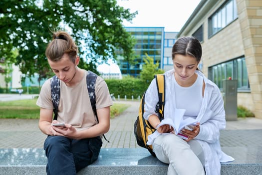 Two high school students guy and girl outdoor, school building background. Education, friendship, youth, adolescence concept