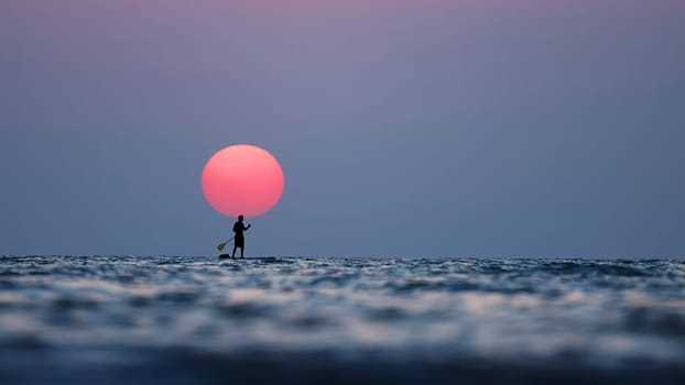 silhouette of a man on the paddleboard against the setting sun. Paddleboard in the sea at sunset, side view . Young man on paddle boarding during a beautiful sunrise. Paddle-boarding by open water.