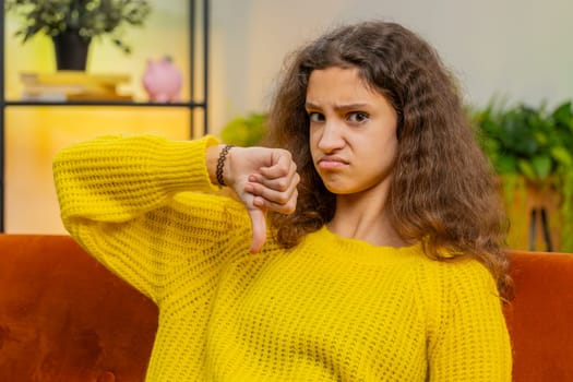 Dislike. Upset child girl showing thumbs down sign gesture, expressing discontent, disapproval, dissatisfied bad work at modern home apartment indoors. Displeased teenager 14-15 years kid in room