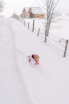Little girl lies in a snowdrift on her stomach near a village road and looks forward. High quality photo