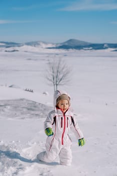 Little smiling girl walks through deep snowdrifts in a mountain valley. High quality photo