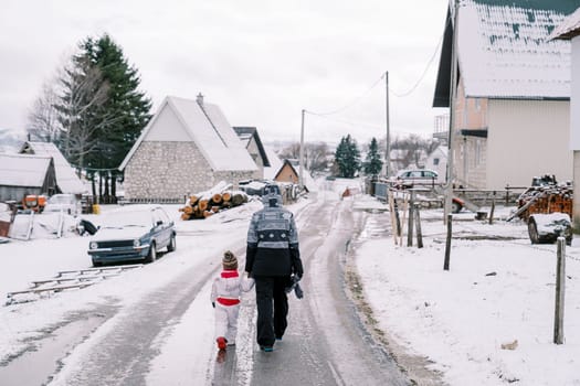 Mom and a little girl walk holding hands along an icy road in a village. Back view. High quality photo