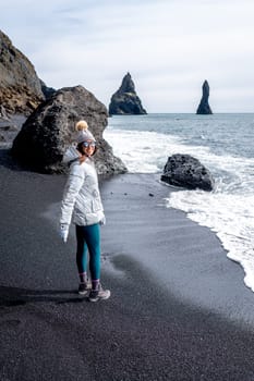 Woman with silver coat and beanie on the black beach of Reynisfjara, Iceland