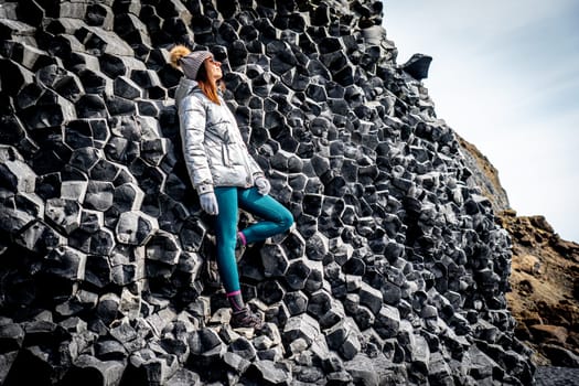 Woman in silver coat and beanie next to basalt formations in Reynisfjara, Iceland