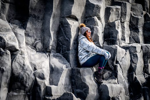 Woman in silver coat and beanie next to basalt formations in Reynisfjara, Iceland