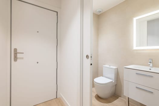 Bathroom with sliding door separating toilet area from corridor. Entrance door to renovated hotel room near fully equipped bathroom