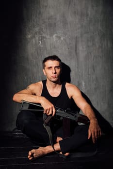 A man sits with a machine gun on a black background in a dark room