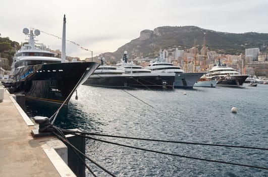 Few huge luxury yachts at the famous motorboat exhibition in the principality of Monaco, Monte Carlo, the most expensive boats for the richest people, mountain and residential complex on background. High quality photo