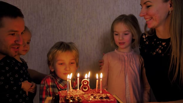In the circle of a large family, the child extinguishes candles on the day of the eighth birthday
