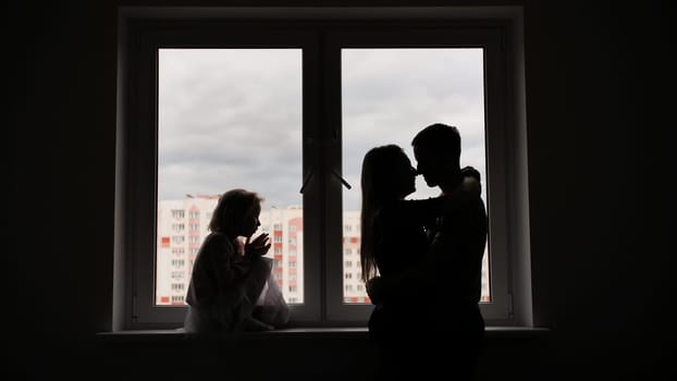 Silhouette of lovers with children on the background of windows from a new apartment