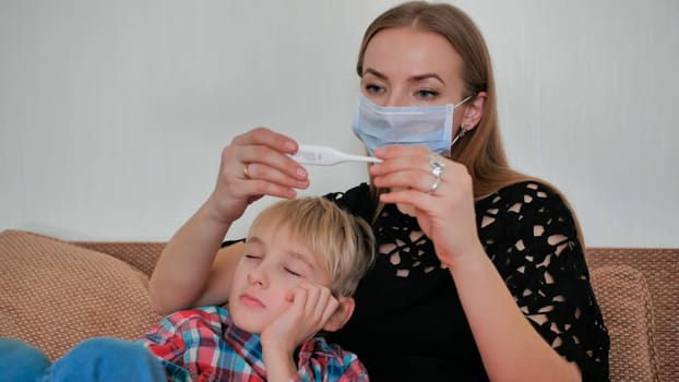 A caring mother measures the temperature of her son with a thermometer