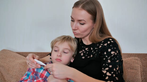 A caring mother measures the temperature of her son with a thermometer