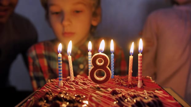 In the circle of a large family, the child extinguishes candles on the day of the eighth birthday