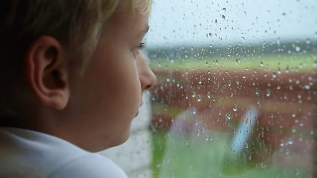 A little boy looks out the window during the rain